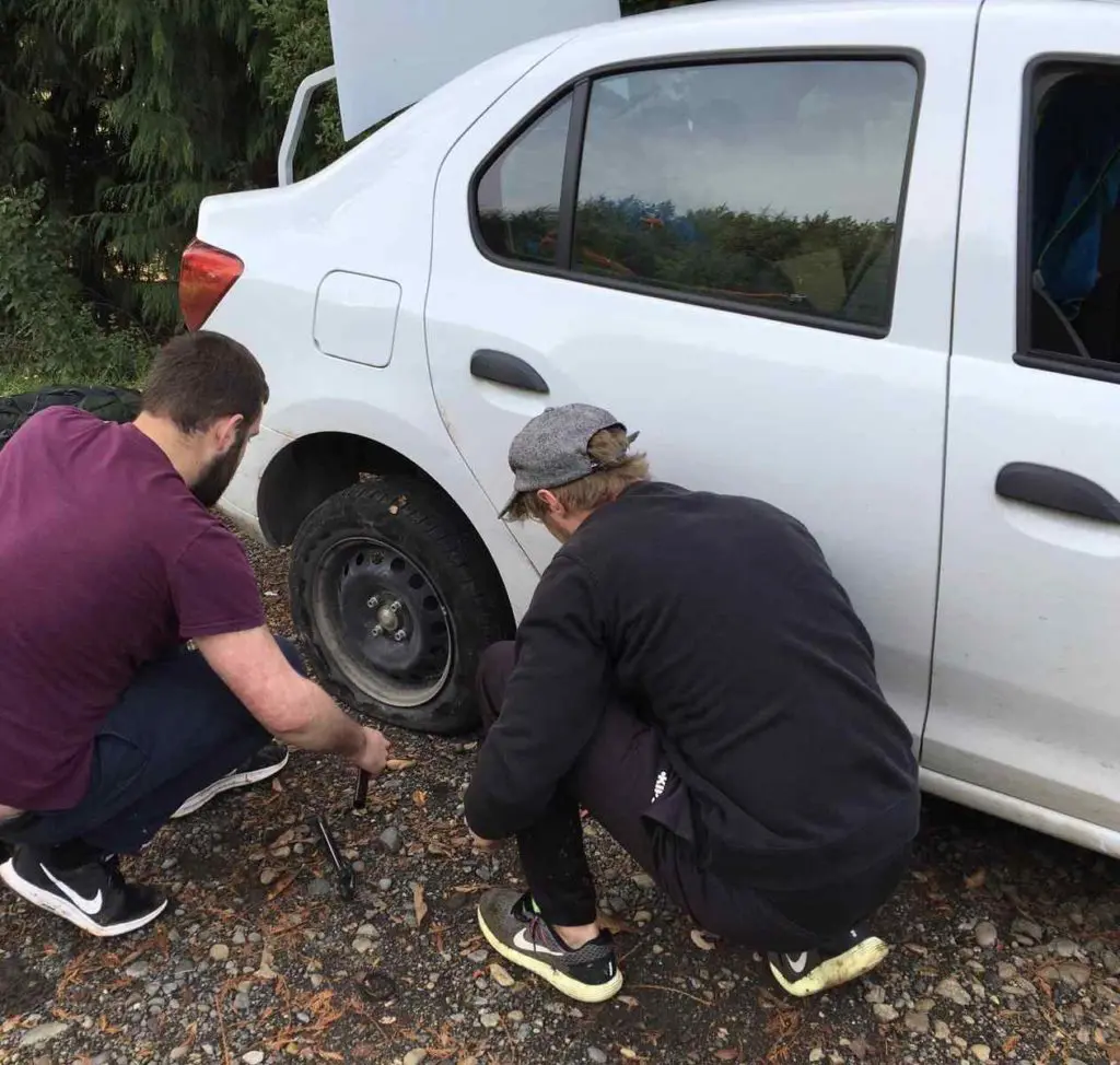 changing a flat tire on a road trip with friends