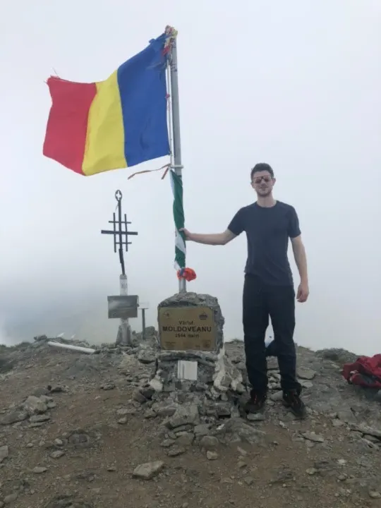 A photo of Iain Salter standing on the summit of  Moldoveanu peak in Romania