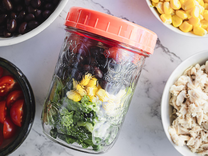 Mexican taco salad in a jar lying down among ingredients