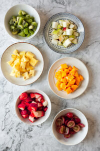 A selection of 6 summer fruits diced and presented in separate bowls on a kitchen surface