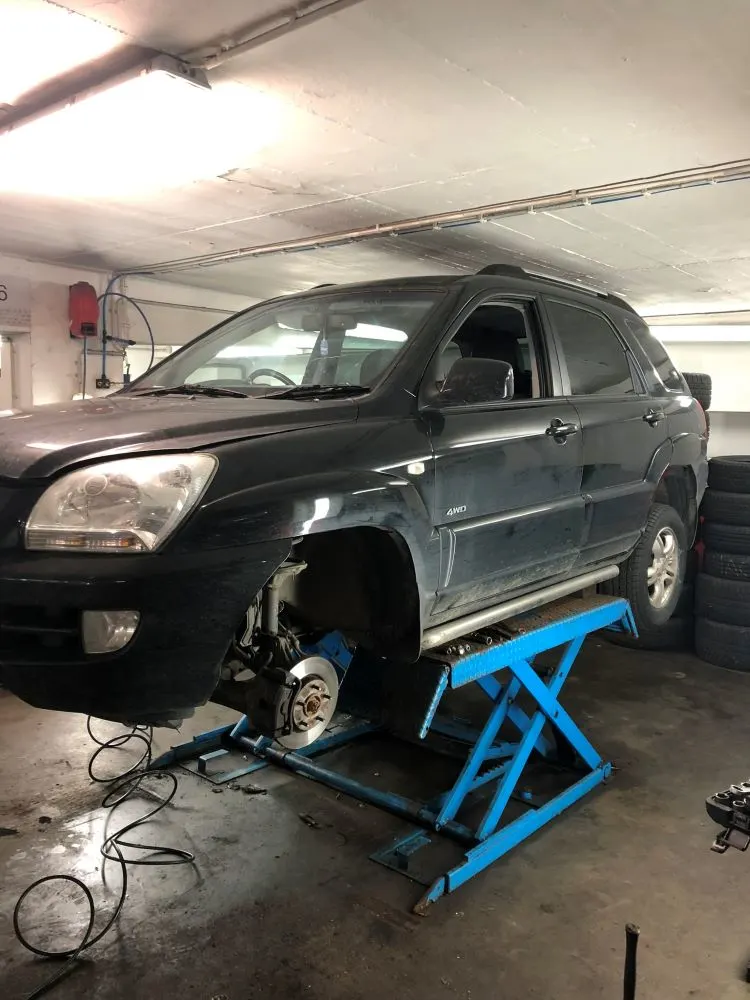 A 2009 black Kia Sportage raised on a car hydraulic lift in a garage with its front right side wheel missing