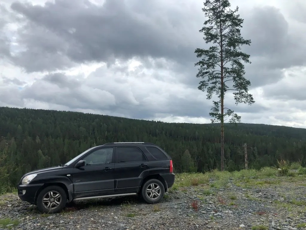 A black 2009 KIA Sportage SUV parked in front of a forest during a road trip around Europe