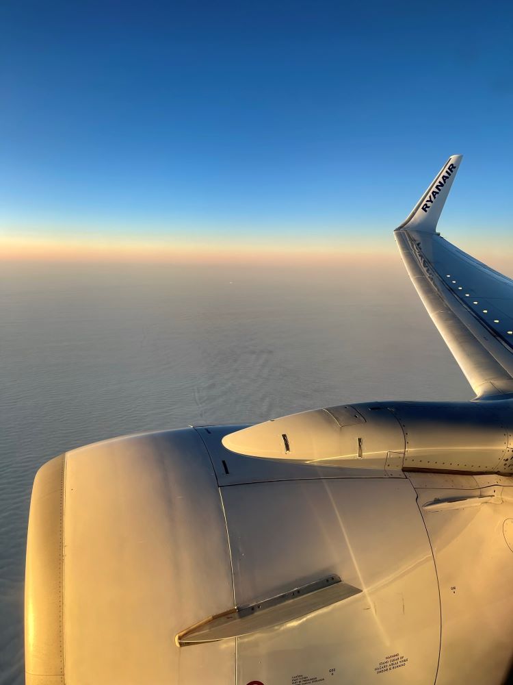 An airplane wing and engine are lit up by sunrise during a flight over the ocean