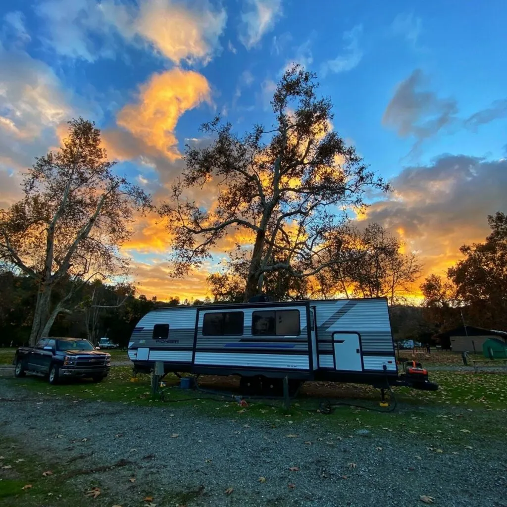 Our RV parked with our truck on the left hand side at sunset in front of two trees