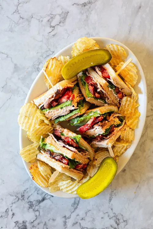 club sandwich that has been sliced into 4 parts is presented on a plate with chips and sliced pickles