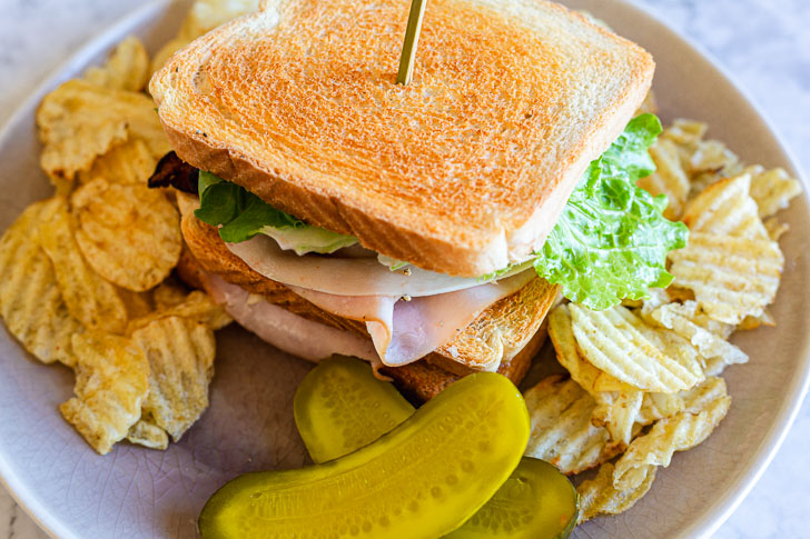 club sandwich presented on a plate with chips and sliced pickles