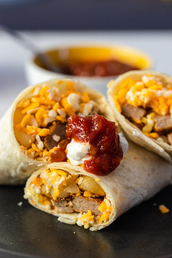 make ahead breakfast burritos sliced in half presented on a black plate with salsa and sour cream