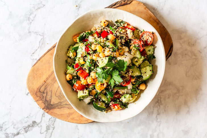 quinoa chickpea salad in a white bowl on top of a wooden chopping board