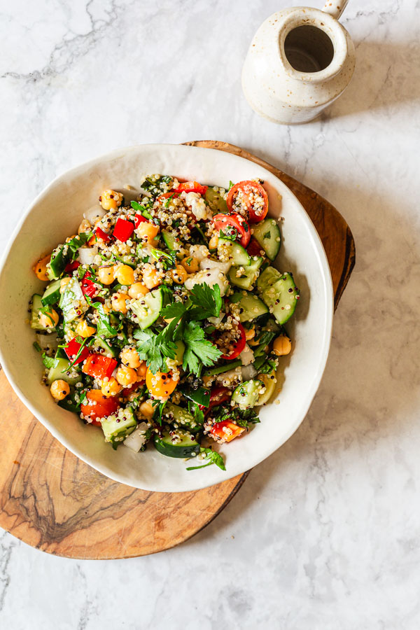 Quinoa Chickpea Salad in  a white bowl on top of a wooden chopping board 